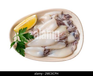 Rohes Tintenfischfilet und Zitrone auf einem Plattenausschnitt. Platte von kleinen Calamaröhren, isoliert auf weißem Hintergrund. Frische Tintenfische zum Kochen kalorienarmer Gerichte. Stockfoto