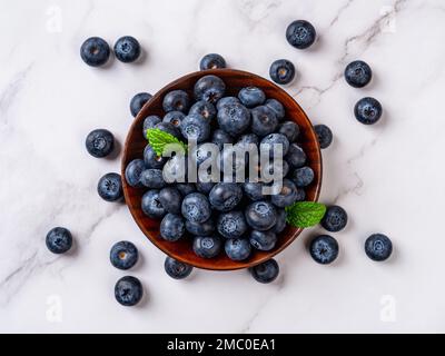 Süße Blaubeeren auf einer Holzplatte über der Marmoroberfläche. Reife saftige Wildbeere zum vegetarischen Dessert. Blaubeere als natürliches Antioxidans für die Entgiftungsdiät Stockfoto