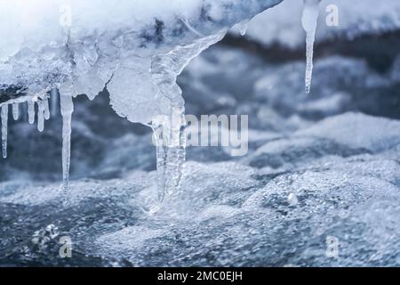 Eis auf dem gefrorenen Fluss, Nahaufnahme, Wasser fließt über Felsen und bildet Wellen und Blasen - Winterhintergrund Stockfoto