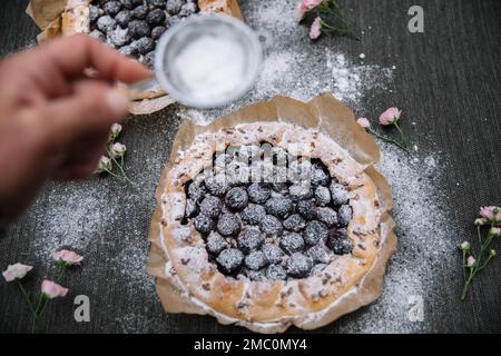 Nahaufnahme einer Frauenhand, die ein Stück Kuchen mit Blaubeeren und Puderzucker hält. Stockfoto