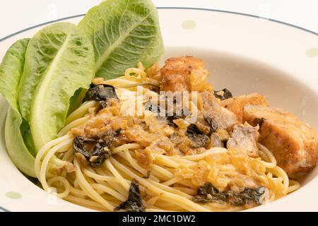 Blick aus der Nähe auf italienische Küche, hausgemachte cremige Spaghetti mit Spinat, Lachs und grünem Gemüse in weißer Keramikschale auf weißem Hintergrund Stockfoto