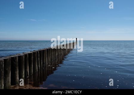 Maritimer Hintergrund, hölzerner Wellenbrecher in ruhiger ostsee vor blauem Himmel Stockfoto