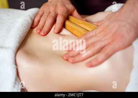 Eine Frau, die eine kreolische Massage im Bauchbereich mit Bambusstäbchen bekommt Stockfoto