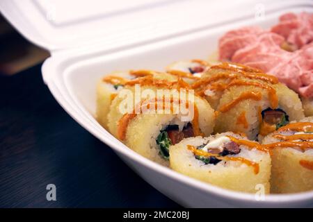 Sushi-Rollen in einem Kunststoffbehälter. Lebensmittellieferung Stockfoto