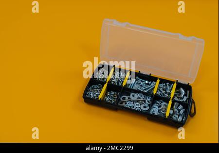 Kofferorganisator mit Schrauben, Muttern und Unterlegscheiben auf gelbem Hintergrund. Befindet sich auf der rechten Seite. Platz für Text oder Logo. Stockfoto