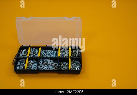 Kofferorganisator mit Schrauben, Muttern und Unterlegscheiben auf gelbem Hintergrund. Befindet sich auf der linken Seite. Platz für Text oder Logo. Stockfoto
