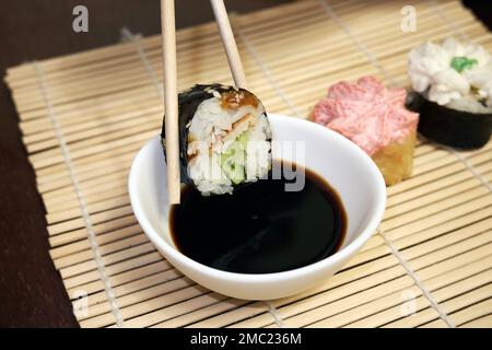 Zwei Essstäbchen nehmen Sushi. Sushi-Brötchen und Sojasoße Stockfoto