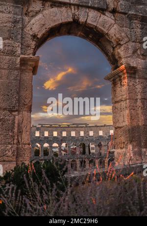 Vertikaler Blick auf die Pula Arena mit dramatischem Himmel. Außenansicht des römischen Amphitheaters während der Goldenen Stunde und des Sonnenuntergangs in Kroatien. Stockfoto