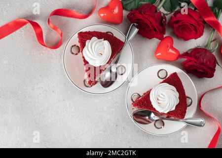 Zwei Portionen Rotsamtkuchen, Rosen und Kerze in Herzform auf grauem Hintergrund, Dessert zum Valentinstag, Kopierbereich Stockfoto