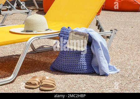 Liegestuhl und Sommerzubehör, Häkeltasche, Strohhut und Lederschuhe am Pool Stockfoto