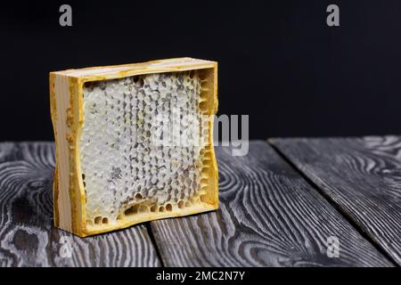 Honig in Waben in einem Holzrahmen. Auf schwarzen Pinienbrettern. Auf schwarzem Hintergrund. Stockfoto