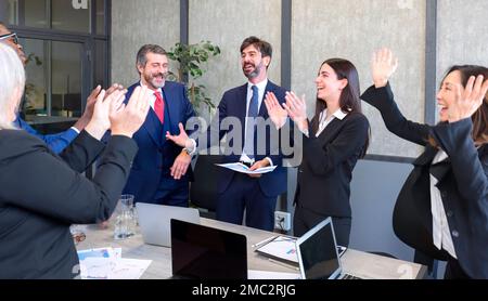 Eine Gruppe multiethnischer Arbeiter, die glücklich und selbstbewusst lächeln. Sie arbeiten mit einem Lächeln im Gesicht zusammen und applaudieren einem von ihnen im Büro Stockfoto