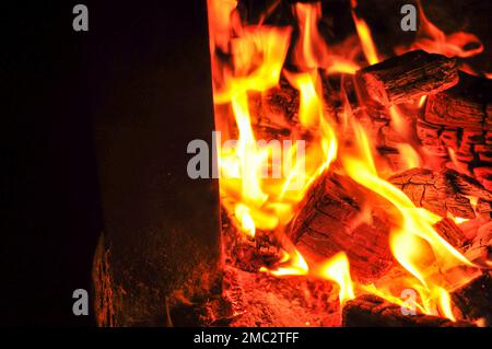 Eine schöne Nahaufnahme in Bewegung von hellem Feuer und schwelenden Kohlen auf dunklem Hintergrund Stockfoto