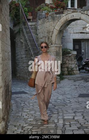 Modische Touristin in seidenbeigefarbenem einfarbigem Outfit in den Straßen der historischen Stadt Trogir, Kroatien Stockfoto