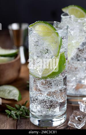 Nahaufnahme von Gin und Tonic Cocktail mit Limettenscheiben und Eis auf einem rustikalen Holztisch Stockfoto