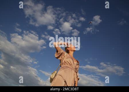 Schöne junge Frau, die die Arme unter blauem Himmel erhebt, Konzept von Freiheit, Glück und Freude Stockfoto