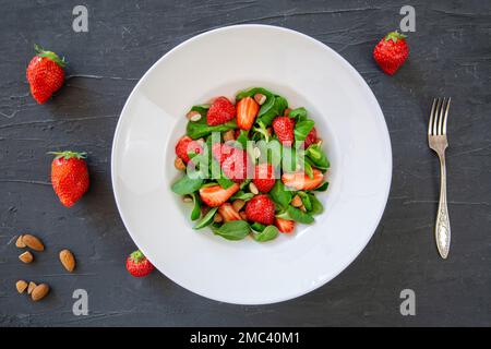 Gesunder Salat mit Nüssen und Beeren auf schwarzem Tisch, Draufsicht. Stockfoto