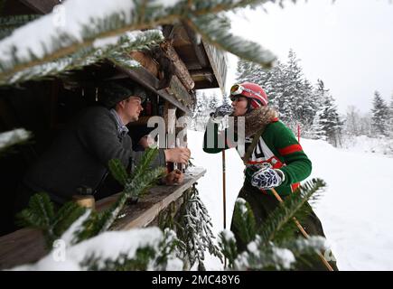 Bayern, Deutschland. 21. Januar 2023. 21. Januar 2023, Bayern, Krün: An der 'Mittelstation' muss ein Teilnehmer mit seinen hölzernen Skiern ohne Kanten beim Skirennen 'Nostalski' im Barmsee-Lift einen Schnaps trinken. Mit alten Holzskiern und Schnürsenkel aus Leder, zumindest aus dem vergangenen Jahrhundert, beginnen die Teilnehmer mit einem lustigen Rennen. Foto: Angelika Warmuth/dpa Credit: dpa Picture Alliance/Alamy Live News Stockfoto