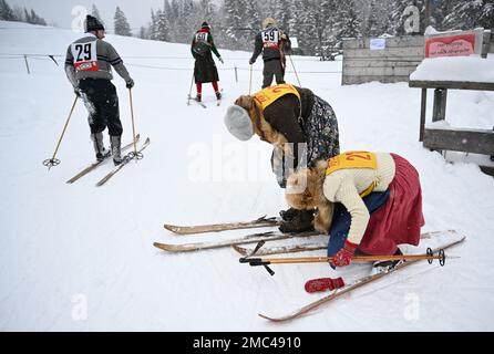Bayern, Deutschland. 21. Januar 2023. 21. Januar 2023, Bayern, Krün: Teilnehmer schnallen sich vor dem „Nostalski“-Skirennen im Barmsee-Lift ihre Holzskier an. Mit alten Holzskiern und Schnürsenkel aus Leder, zumindest aus dem vergangenen Jahrhundert, beginnen die Teilnehmer mit einem lustigen Rennen. Foto: Angelika Warmuth/dpa Credit: dpa Picture Alliance/Alamy Live News Stockfoto