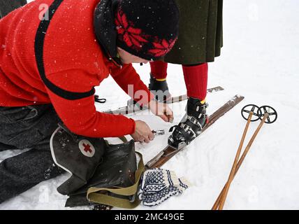 Bayern, Deutschland. 21. Januar 2023. 21. Januar 2023, Bayern, Krün: Ein Teilnehmer passt die Bindung eines anderen Teilnehmers an Holzskiern vor dem „Nostalski“-Skirennen im Barmsee-Lift an. Mit alten Holzskiern und Schnürsenkel aus Leder, zumindest aus dem vergangenen Jahrhundert, starten die Teilnehmer ein lustiges Rennen. Foto: Angelika Warmuth/dpa Credit: dpa Picture Alliance/Alamy Live News Stockfoto