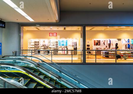 Internationaler Flughafen Tokio Haneda. Innenraum. Rolltreppe im Vordergrund mit Hintergrund des Modegeschäfts Uni Qlo im Terminal 1. Stockfoto