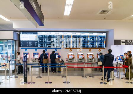 Tokio Haneda International Airport. Terminal 1 Interieur. Menschen mit einer Reihe von Bus Ticket Maschinen A und B, mit beleuchtetem Zeitplan vor. Stockfoto
