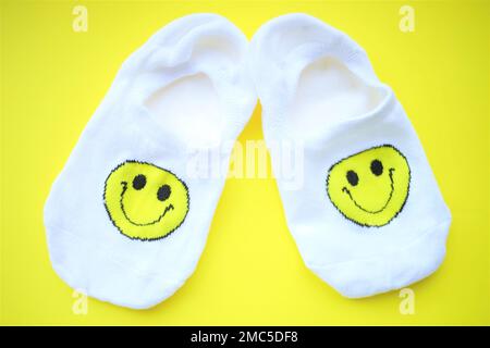 Ein Paar weiße Socken mit einem Smiley auf einem gelben Tisch. Stockfoto