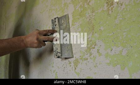 Unebenheiten und Rückstände von Farbe und Putz mit einem Spachtel abkratzen, die Oberfläche einer Raumwand reinigen und vorbereiten, bevor Tapeten angebracht werden Stockfoto