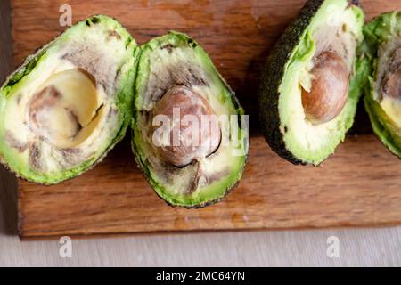 Verfaulte Avocadofrüchte auf Holzhintergrund in zwei Hälften geschnitten Stockfoto