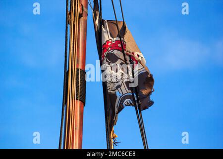 Die Piratenflagge oder die Jolly Roger - alte schäbige schwarze Flagge mit einem Schädel, der auf dem Mast eines Segelschiffs winkt Stockfoto