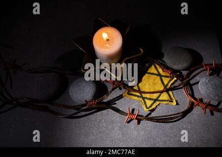 Holocaust-Gedächtnisfeiertag. Stacheldraht, Steine, gelber Stern und brennende Kerze auf schwarzem Hintergrund Stockfoto