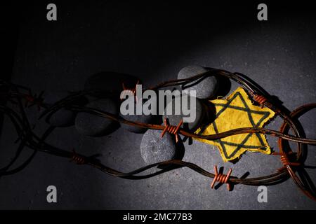 Holocaust-Gedächtnisfeiertag. Stacheldraht, Steine und gelber Stern auf dunklem Hintergrund Stockfoto
