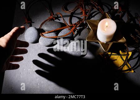Holocaust-Gedächtnisfeiertag. Stacheldraht, Steine, gelber Stern und brennende Kerze auf schwarzem Hintergrund Stockfoto