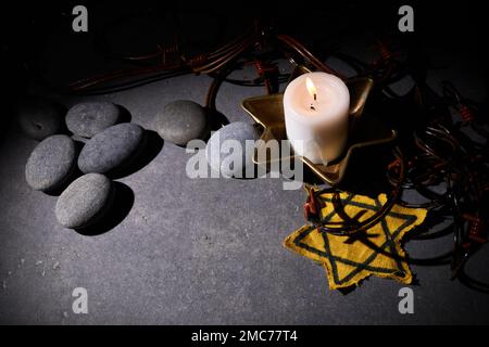 Holocaust-Gedächtnisfeiertag. Stacheldraht, Steine, gelber Stern und brennende Kerze auf schwarzem Hintergrund Stockfoto