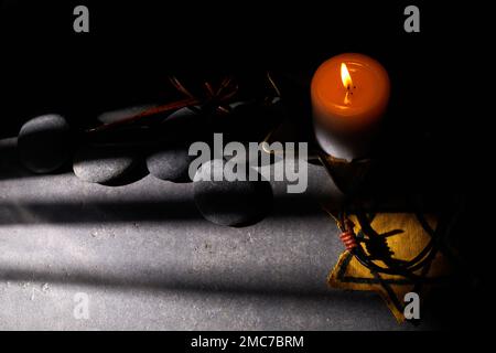 Holocaust-Gedächtnisfeiertag. Stacheldraht, Steine, gelber Stern und brennende Kerze auf schwarzem Hintergrund Stockfoto