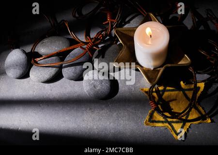 Holocaust-Gedächtnisfeiertag. Stacheldraht, Steine, gelber Stern und brennende Kerze auf schwarzem Hintergrund Stockfoto