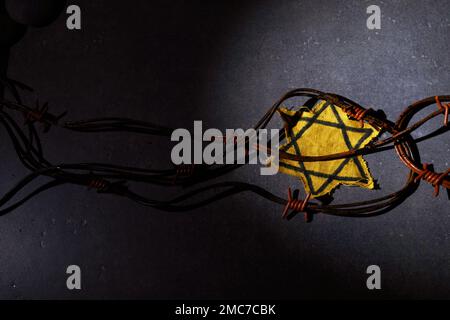 Holocaust-Gedächtnisfeiertag. Stacheldraht, Steine und gelber Stern auf dunklem Hintergrund Stockfoto