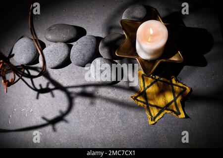 Holocaust-Gedächtnisfeiertag. Stacheldraht, Steine, gelber Stern und brennende Kerze auf schwarzem Hintergrund Stockfoto