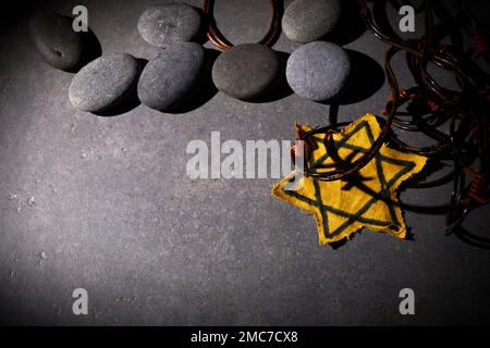 Holocaust-Gedächtnisfeiertag. Stacheldraht, Steine und gelber Stern auf dunklem Hintergrund Stockfoto