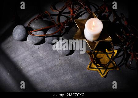 Holocaust-Gedächtnisfeiertag. Stacheldraht, Steine, gelber Stern und brennende Kerze auf schwarzem Hintergrund Stockfoto
