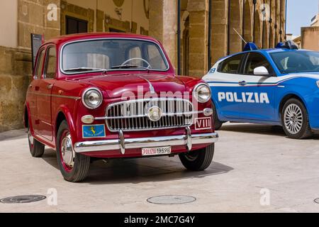 Ein roter Fiat 1100 Polizia Stradale parkt vor einem neuen blauen Polizeiauto auf einem Platz in Marsala. Stockfoto