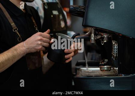 Barista schäumt Milch auf, um Kaffee zuzubereiten. Barista Hände vor der Kaffeemaschine Stockfoto