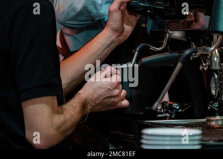 Barista schäumt Milch auf, um Kaffee zuzubereiten. Barista Hände vor der Kaffeemaschine Stockfoto