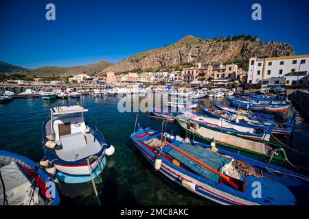 Fischerboote gehen vor Anker im Hafen und im Yachthafen der kleinen Stadt Mondello, der Felswand des Berges Mt. Gallo hinter den Häusern. Stockfoto