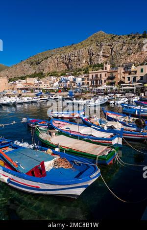 Fischerboote gehen vor Anker im Hafen und im Yachthafen der kleinen Stadt Mondello, der Felswand des Berges Mt. Gallo hinter den Häusern. Stockfoto