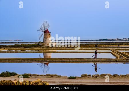 Wasserbecken, Salinen und eine Windmühle bei der Mozia Salz Works, ein Arbeiter läuft auf einem Damm. Stockfoto