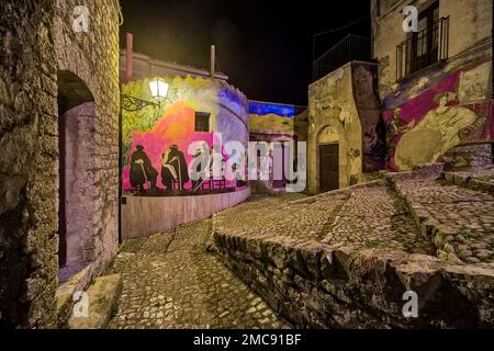 Kleine Straße mit Treppen, Graffiti an einer Wand und eine Laterne in der Stadt Prizzi, beleuchtet bei Nacht. Stockfoto