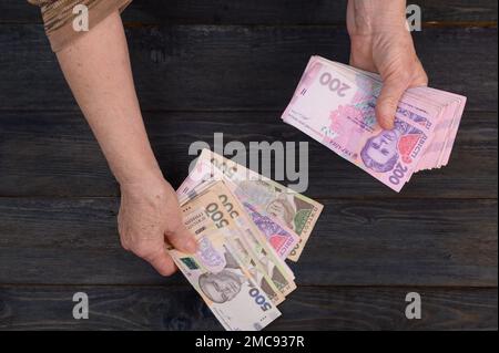 Eine ältere Frau zählt ihr Geld auf einem Holztisch Stockfoto