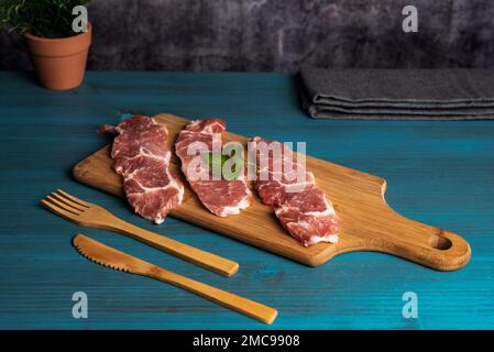 Iberische Schweinelende Steaks auf einem Schneidebrett, auf einem rustikalen Holztisch. Stockfoto