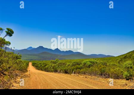 Unbefestigte Straße durch die Wildnis, die an einem sonnigen Sommertag zu den scharf definierten Bergen des Stirling Range-Nationalparks in Westaustralien führt Stockfoto